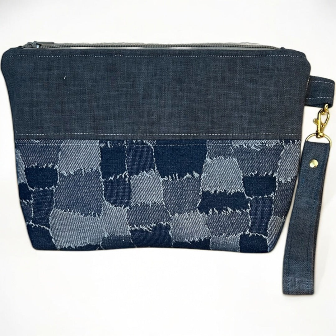 Handmade denim wristlet with a patchwork-effect design in deep and faded blue tones. Crafted from upcycled fabric, this eco-friendly clutch features a detachable strap, secure zipper closure, and gold-tone hardware, making it a stylish and sustainable choice for everyday essentials.