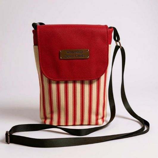 Front view of the red and cream striped mini crossbody bag with red flap closed and Watership Down Crafts label visible, featuring an adjustable black strap.