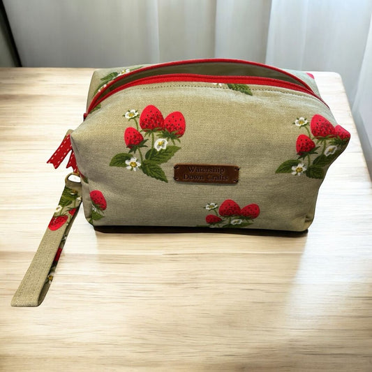 Handmade makeup bag with red zip and wrist strap, featuring Sophie Allport strawberry fabric, made by Watership Down Crafts.