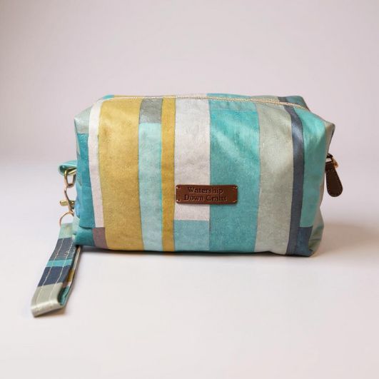 Front view of a boxed makeup pouch in soft aqua, mustard, and cream striped fabric with a matching wrist strap and Watership Down Crafts label.
