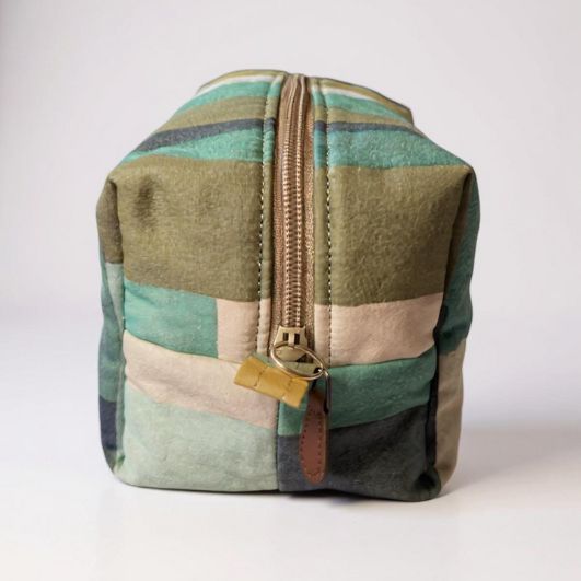 Side view of the striped pouch showing its upright boxed structure, zip closure, and subtle colour variation across the stripes.