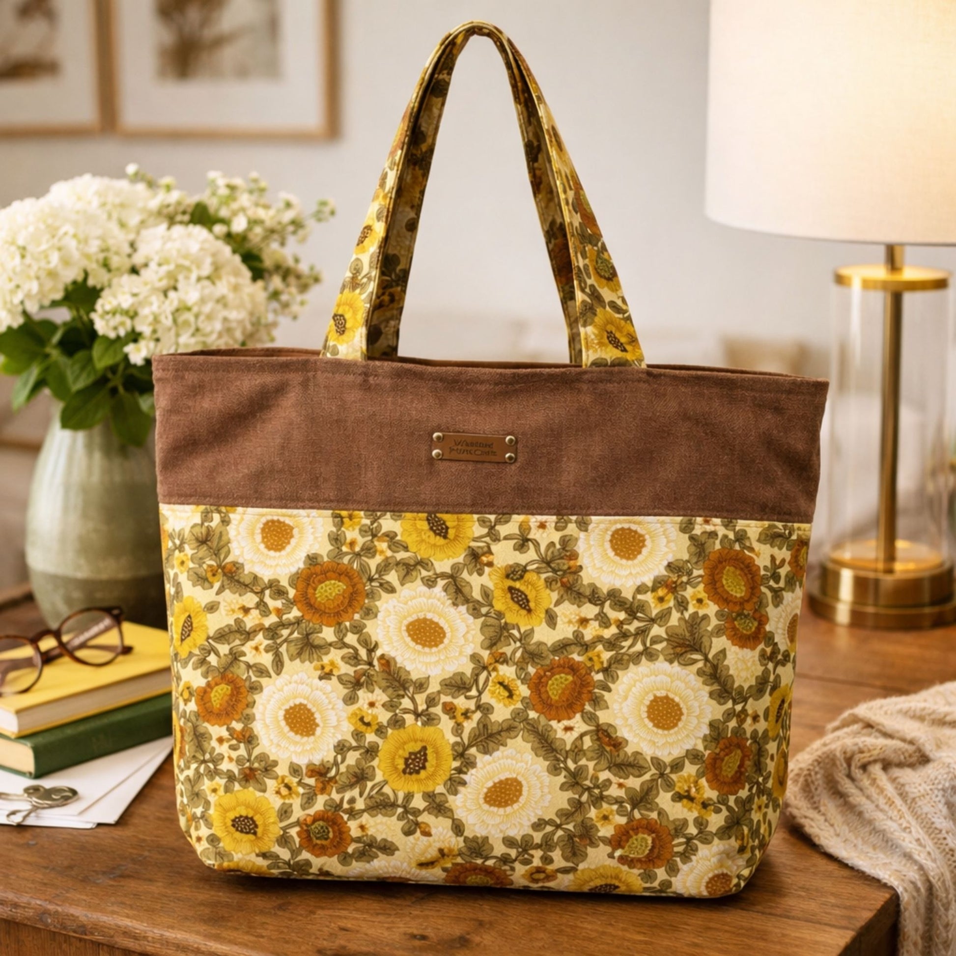 Floral-patterned tote bag on a wooden surface with a lamp and flowers in the background