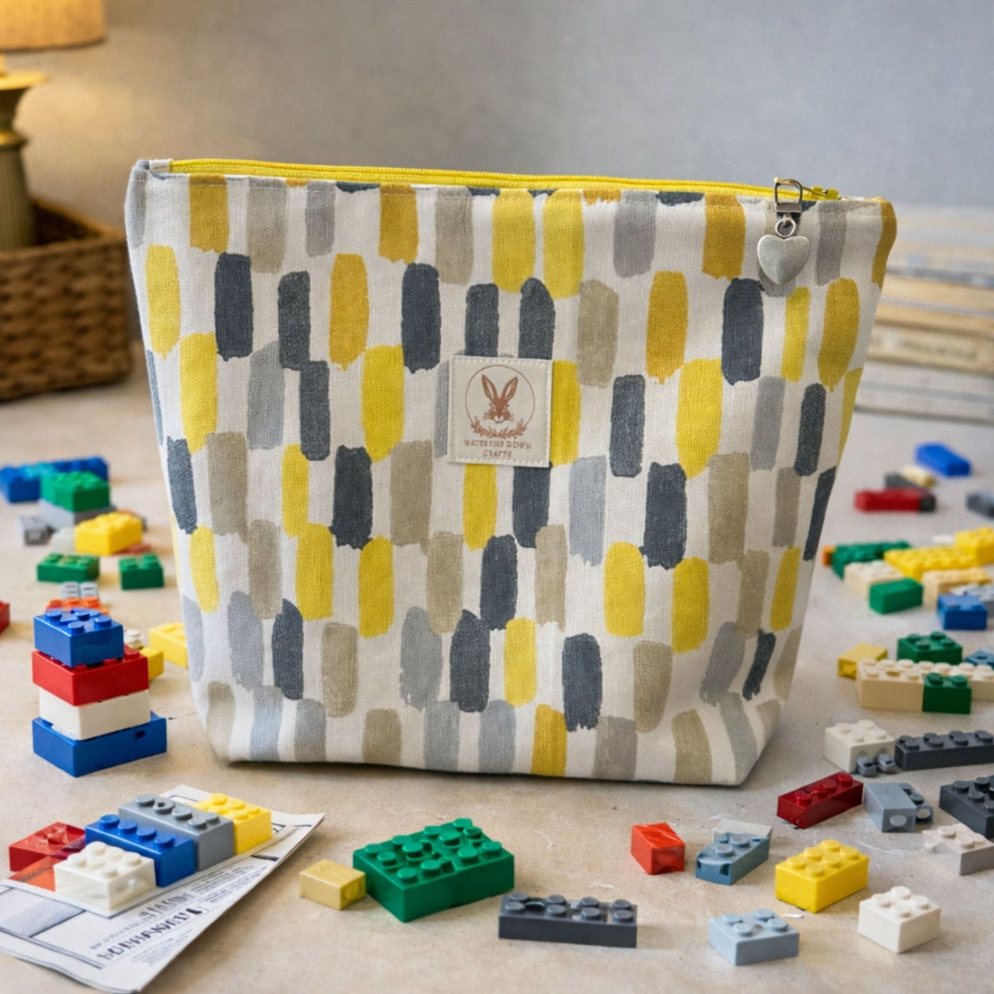 Patterned pouch with a brand logo surrounded by colorful building blocks on a wooden surface.